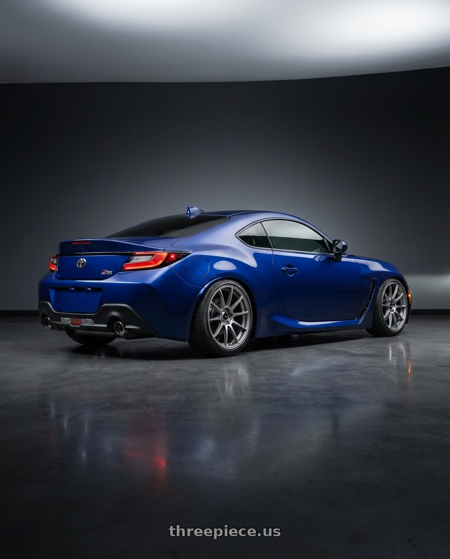 2023 Toyota GR86 base Tureno blue with Enkei Triumph 5x100 18x8.5+45 Storm Gray wheels rear three quarter view square tires