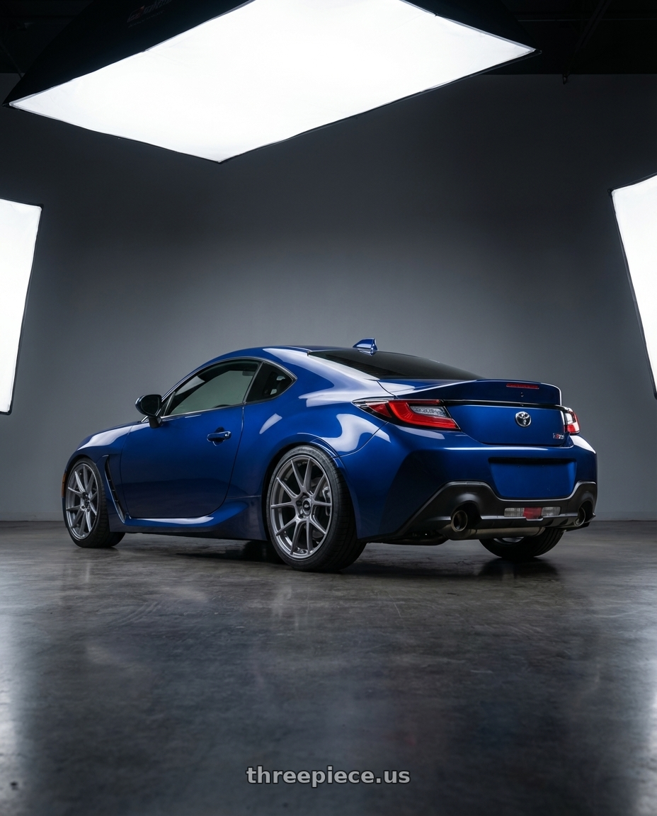 2023 Toyota GR86 base Tureno blue with Enkei TS-V 5x100 18x8.5+45 Storm Grey wheels rear three quarter view square tires